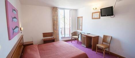 A hotel room with a bed, a desk, a chair, a television, and a window with curtains.