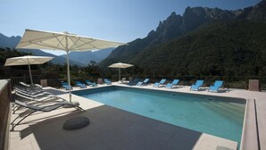 A pool with lounge chairs and umbrellas, surrounded by mountains. - Hotel Kalliste (Ota)
