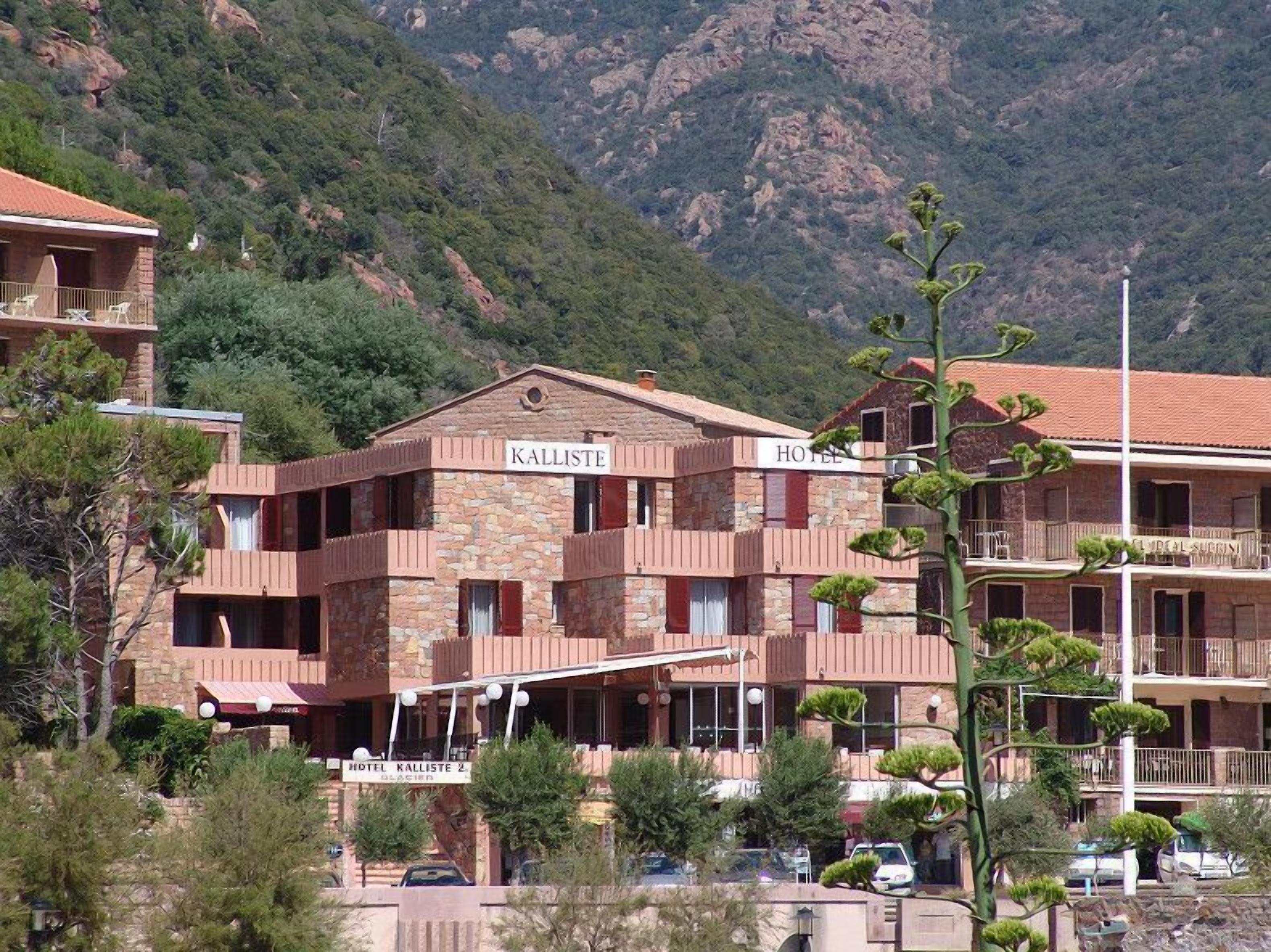 Un hôtel appelé « Kalliste », doté d’une façade en pierre, de nombreux balcons et surplombant un paysage montagneux.