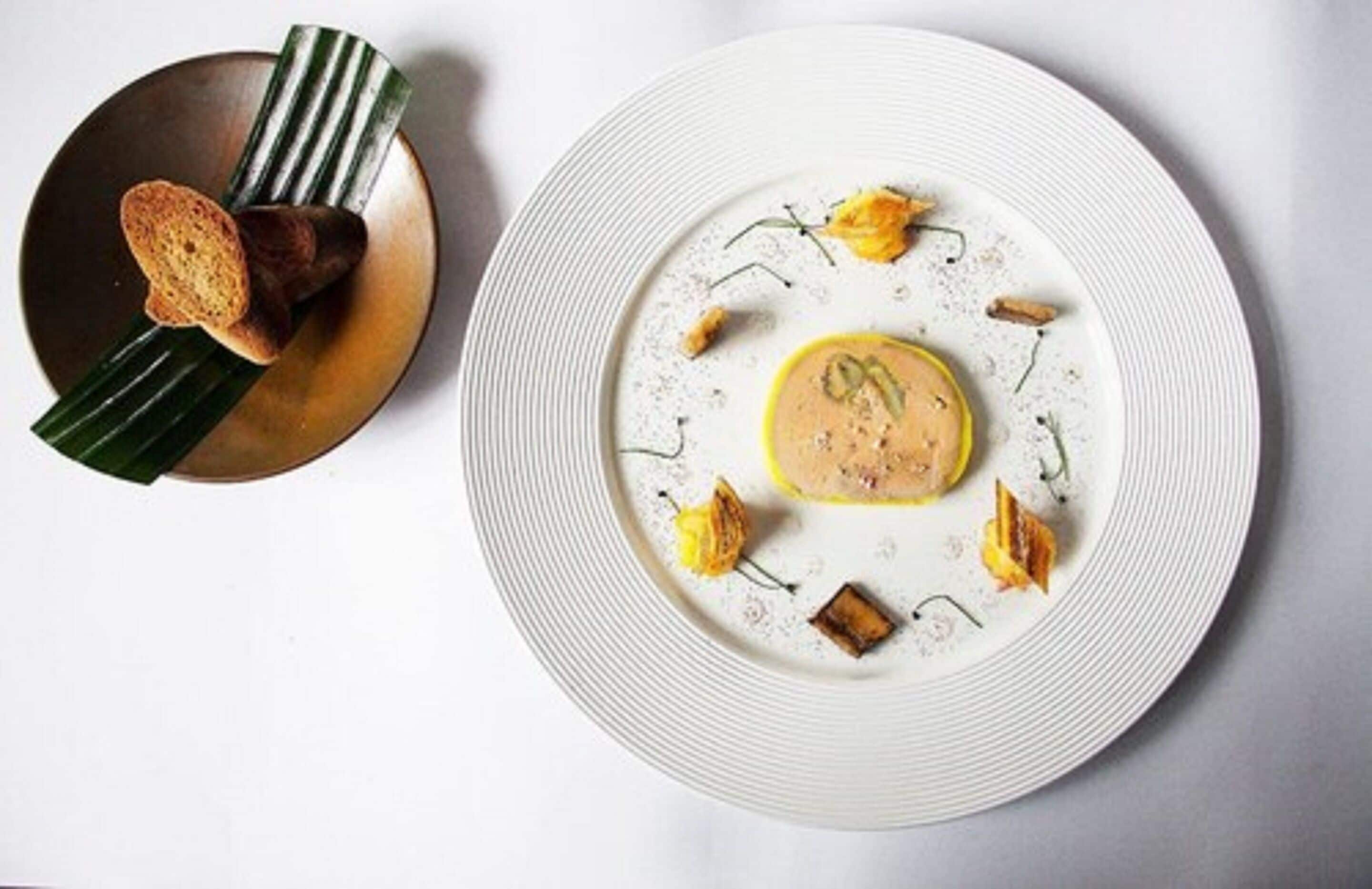 Une assiette blanche avec un élément jaune au centre, entouré de petits morceaux et de feuilles vertes.