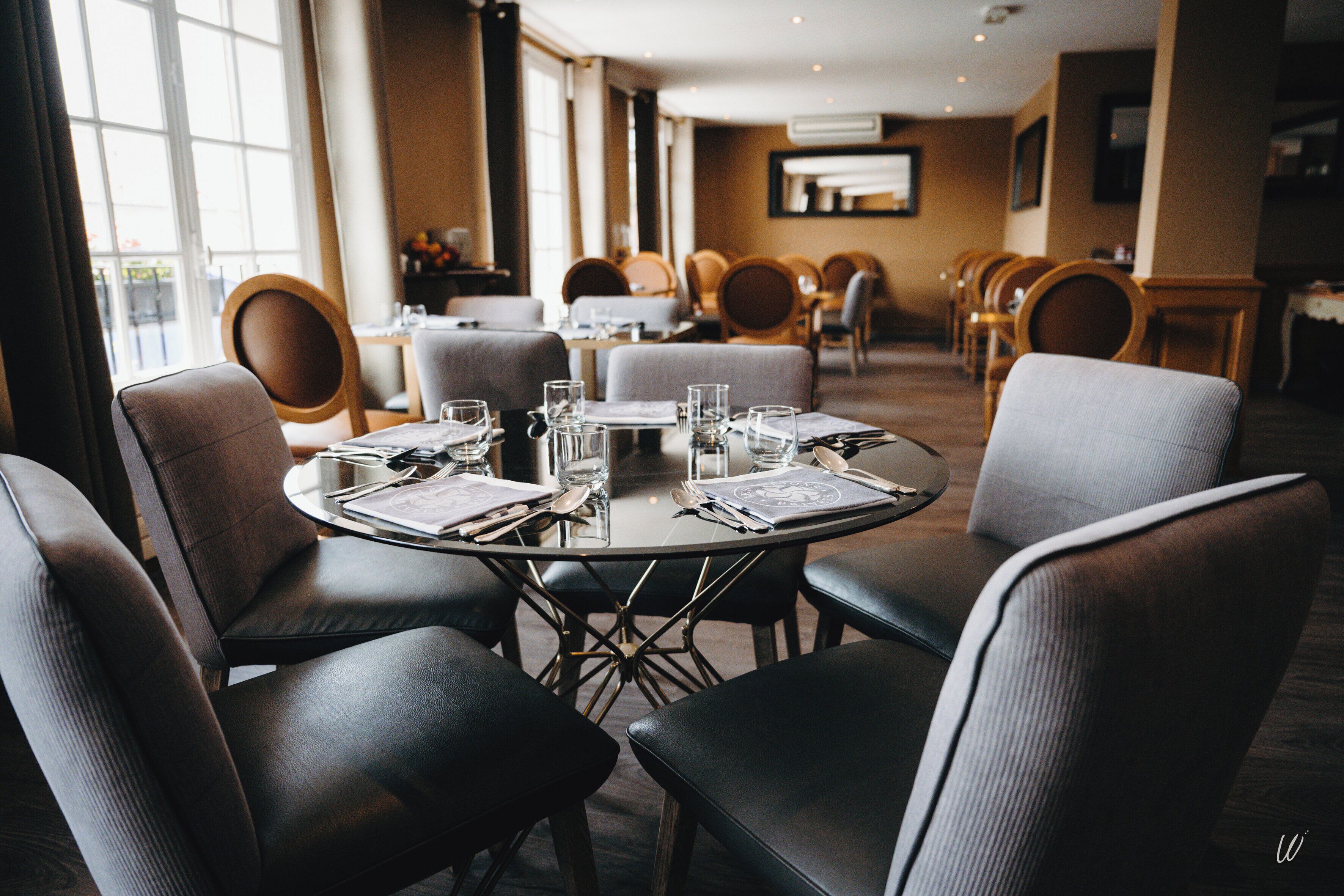 A dining area with round tables set for four, surrounded by upholstered chairs.
