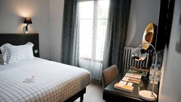 A hotel room with a bed, a desk, a lamp, and a window with curtains.