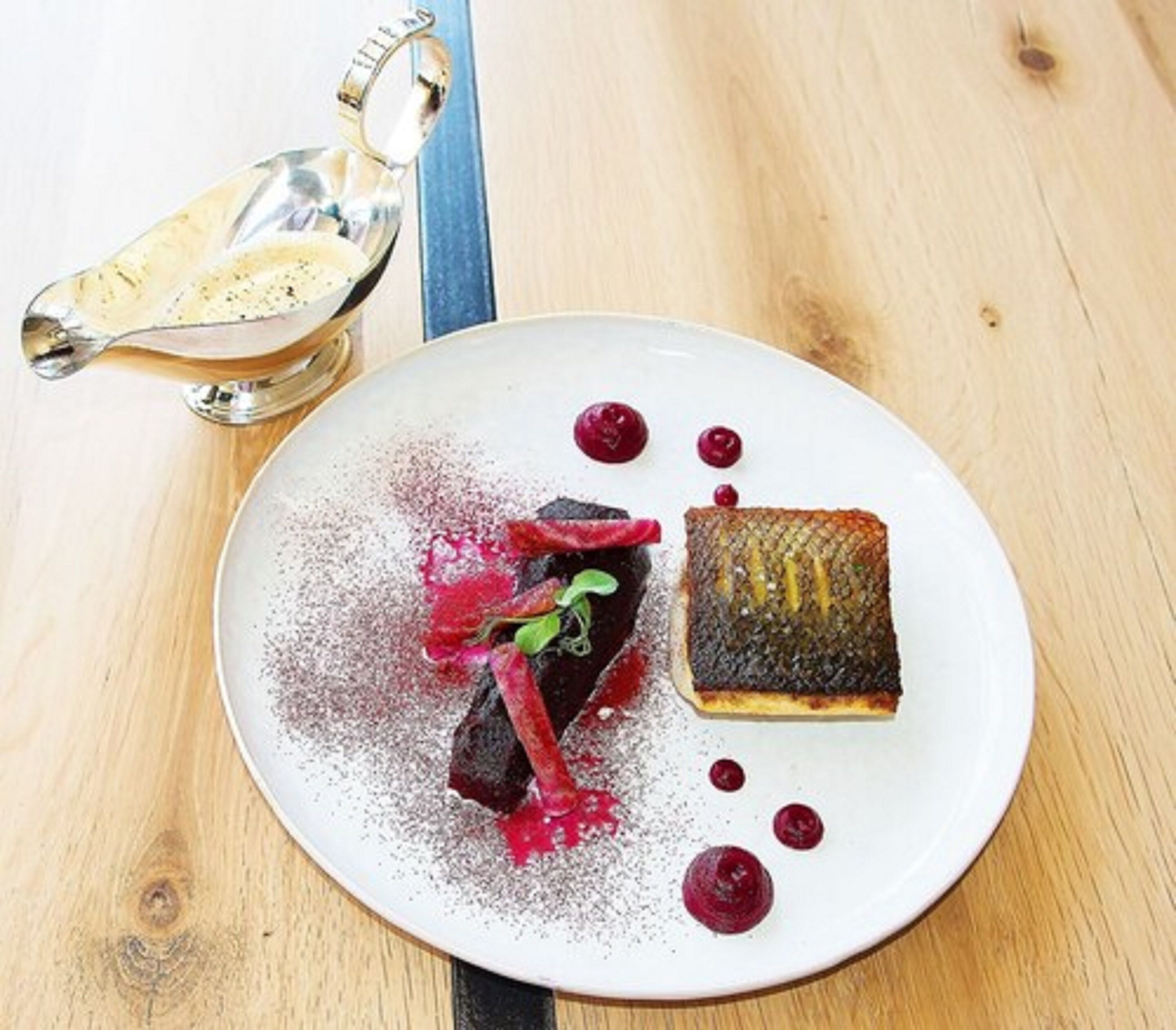 A dessert plate with a cake, berries, and a dusting of powder on a wooden table.