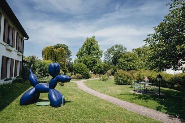 Un jardín con una escultura azul, un sendero y un edificio con contraventanas.