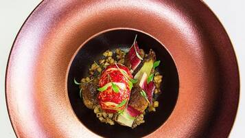 Une assiette de couleur cuivrée avec un plat au centre, une cuillère garnie d’une herbe verte et un petit récipient en verre.