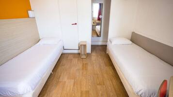 A room with two single beds, a wooden floor, a white door, and a small wooden stool.