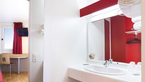 A modern bathroom with a white sink, mirror, and red accents. - Hotel Premiere Classe Cherbourg - Tourlaville (Cherbourg-en-Cotentin)