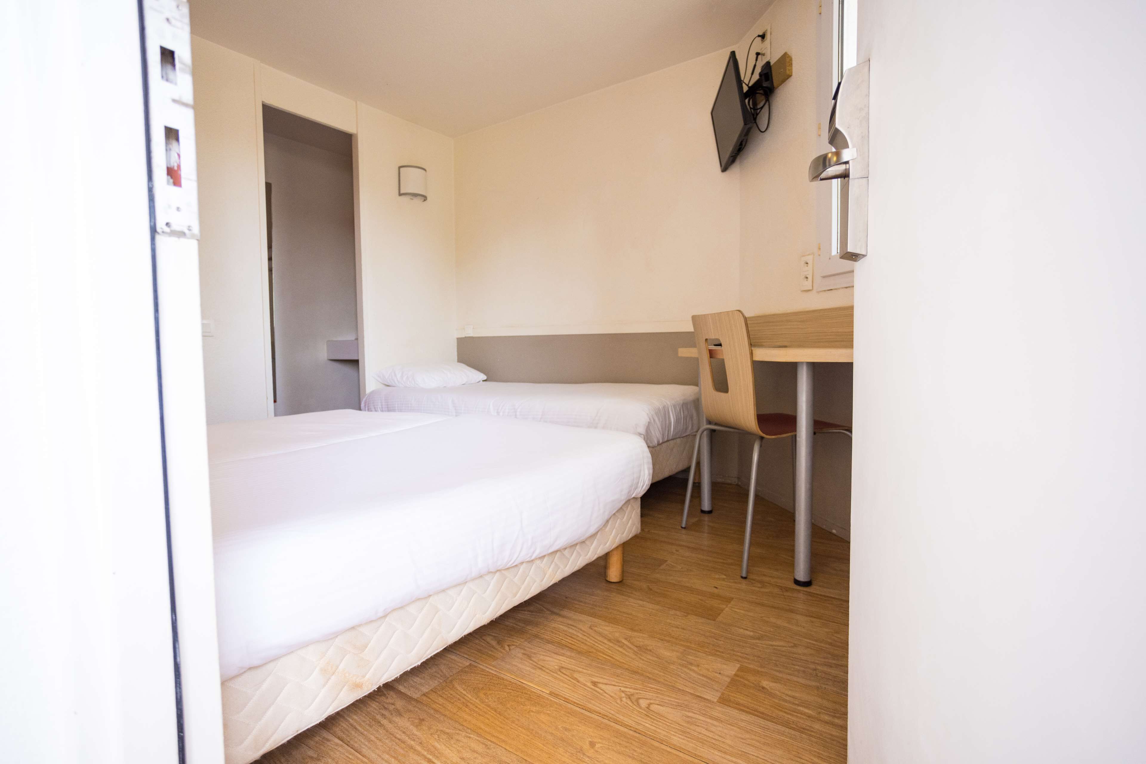 Ein Hotelzimmer mit zwei Einzelbetten, einem Schreibtisch und einem Stuhl.