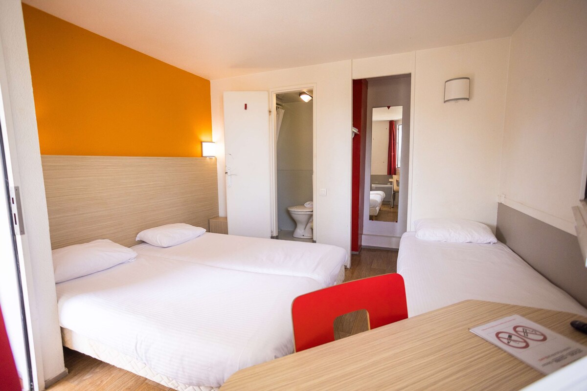 A hotel room with two beds, a wooden table, and a bathroom visible through an open door.