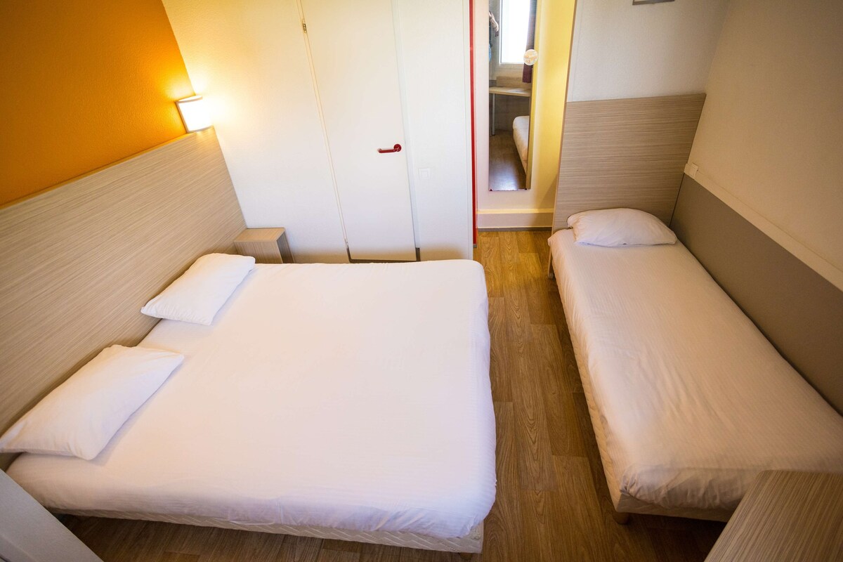A hotel room with two single beds, a wooden floor, a white door, and a mirror on the wall.