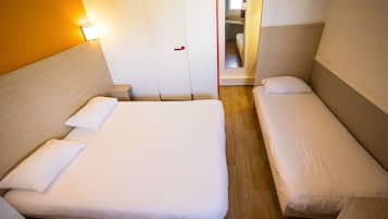 Ein Hotelzimmer mit zwei Einzelbetten, Holzboden, einer weißen Tür und einem Spiegel an der Wand.
