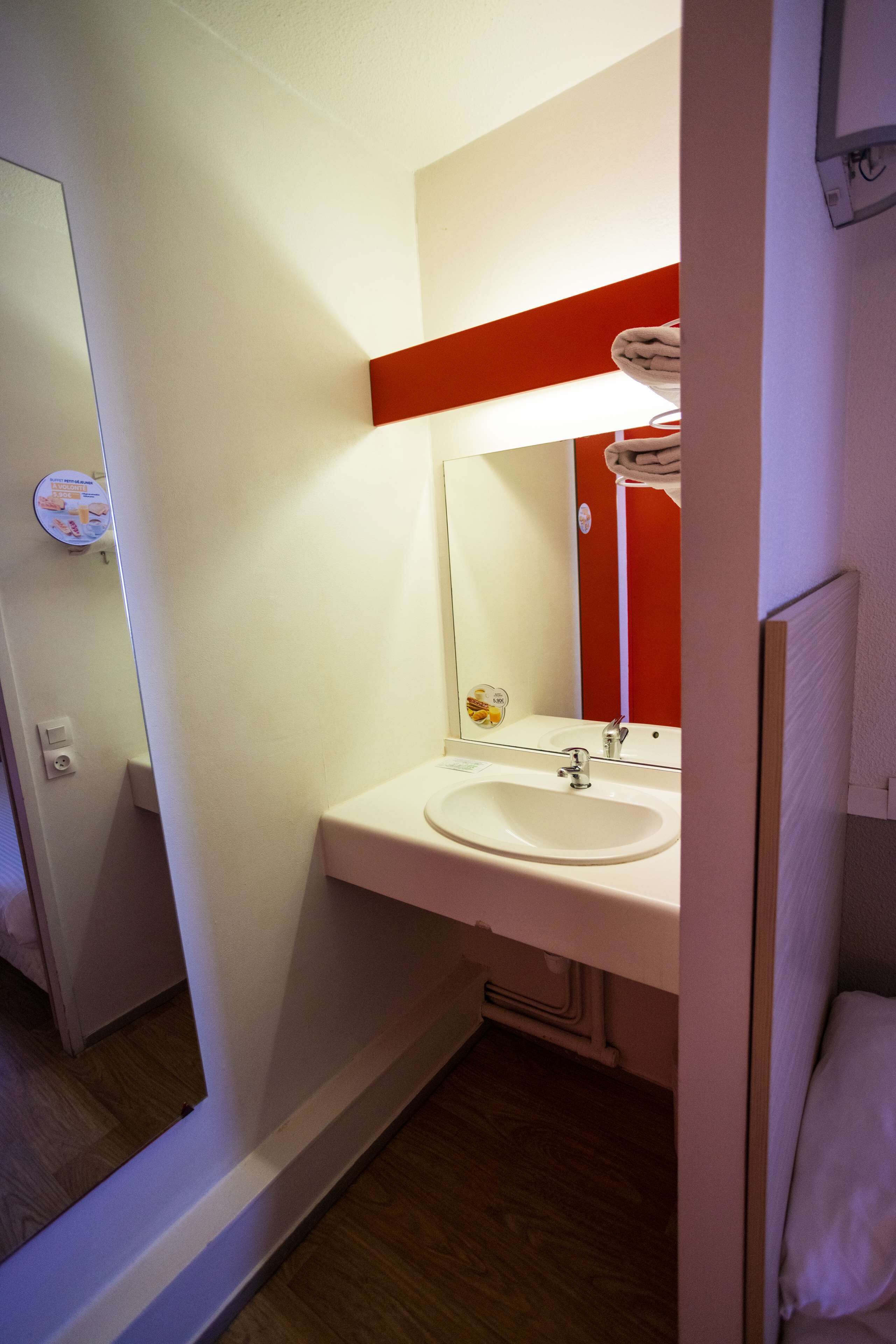 A compact bathroom with a white sink, a mirror, and a red accent wall.