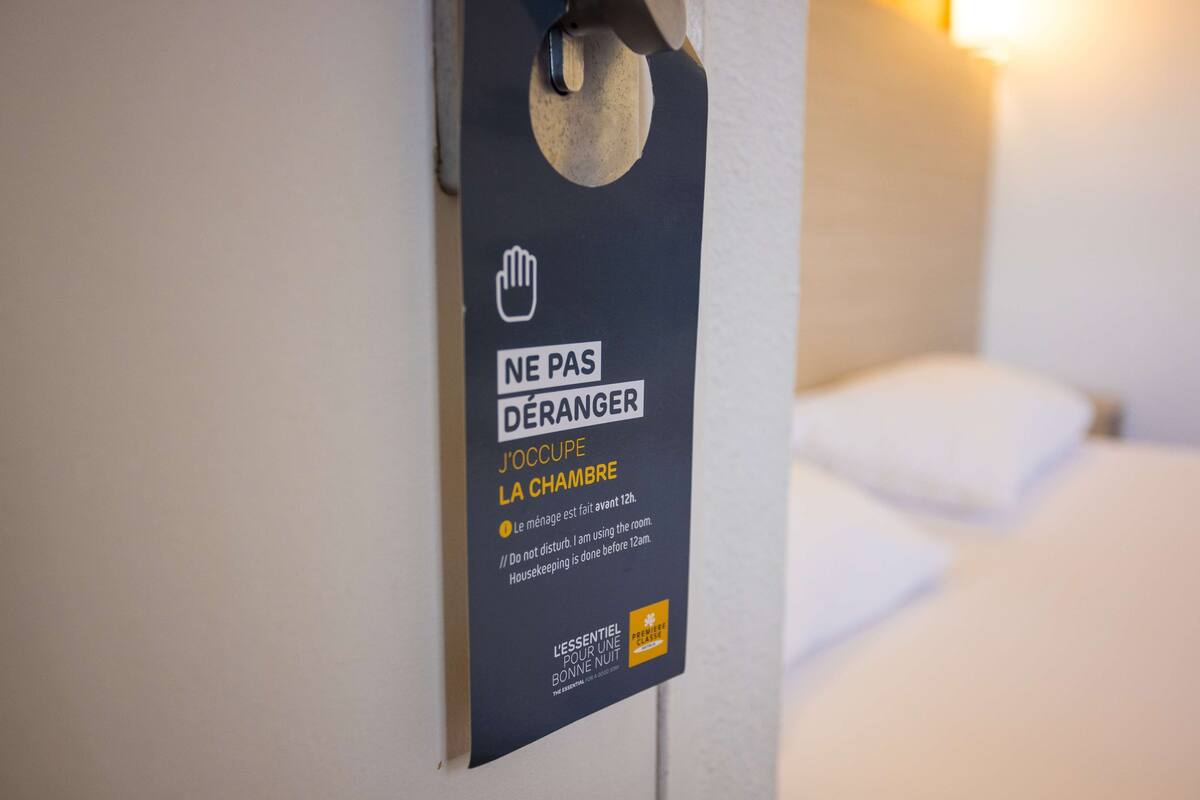 A hotel room door with a sign indicating housekeeping is done before 12am.