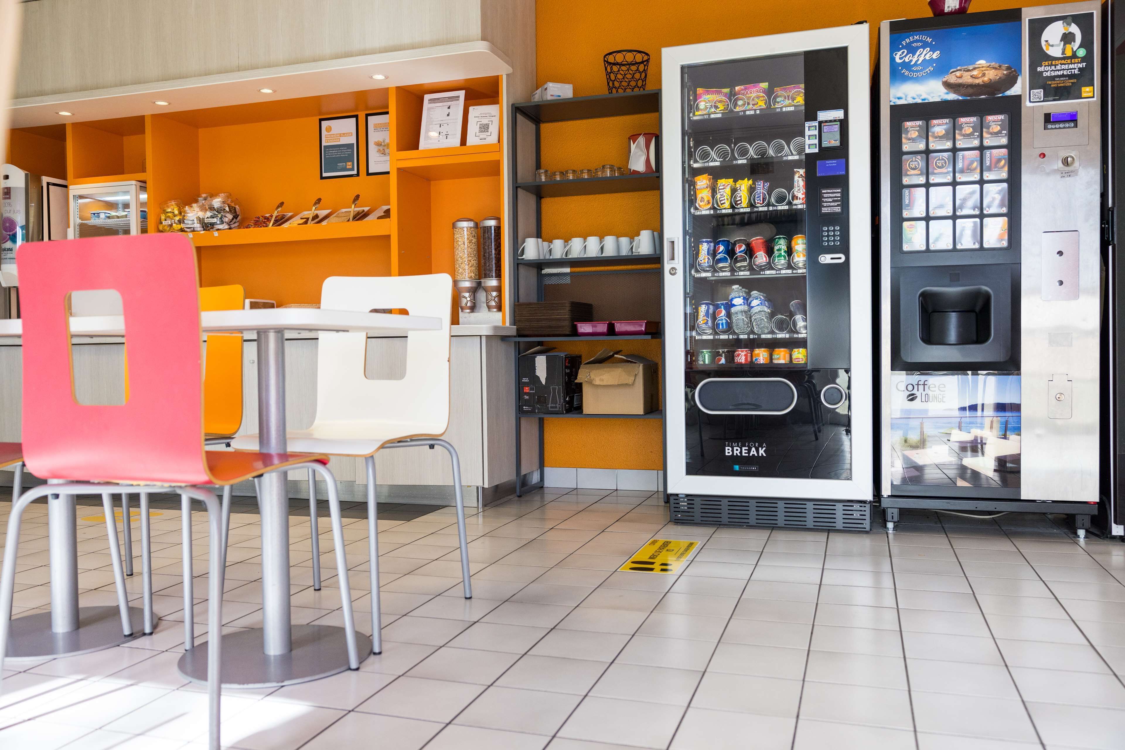 A coffee shop interior with seating, a coffee vending machine, and shelves stocked with snacks and beverages.