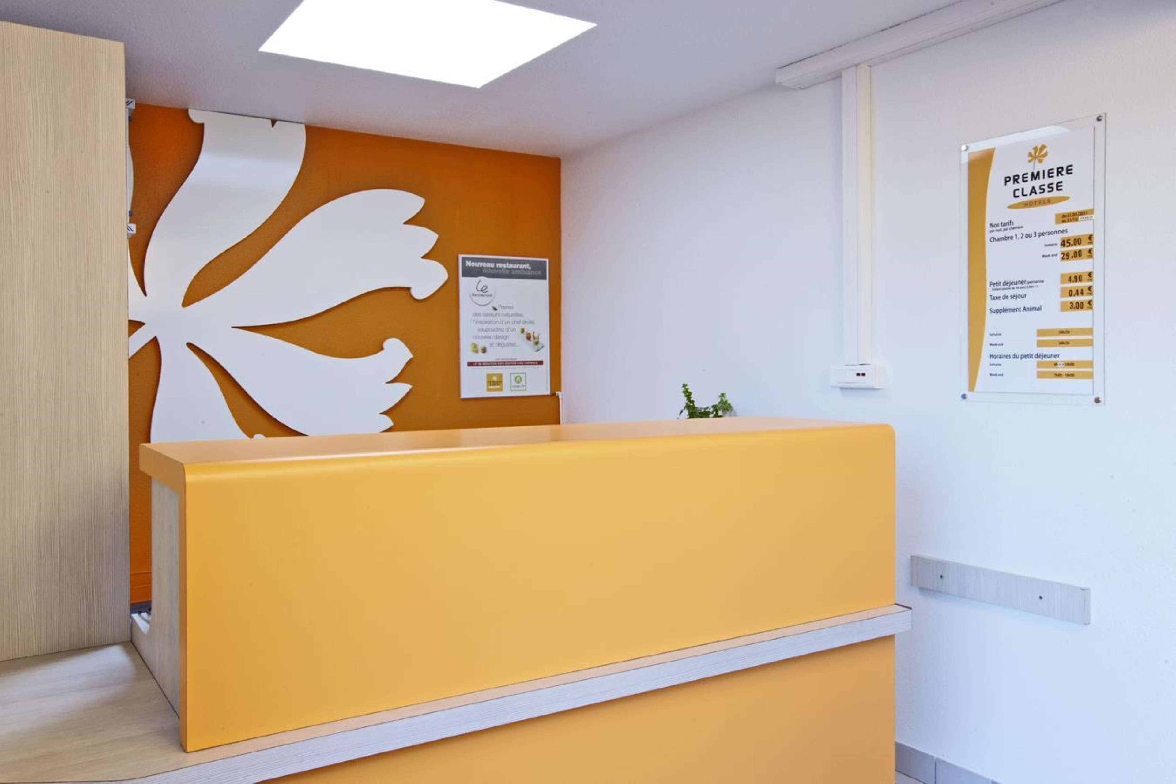 Un comptoir d’accueil avec un plan de travail jaune et un panneau mural décoratif blanc.