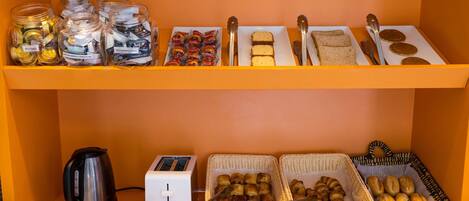 A breakfast buffet with various food items, a kettle, toaster, and baskets of pastries.