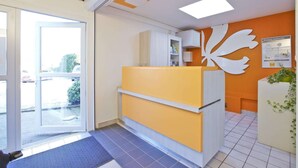 A reception area with a glass door entrance, a reception desk, and a wall-mounted decorative piece. - Hotel Premiere Classe Cherbourg - Tourlaville (Cherbourg-en-Cotentin)