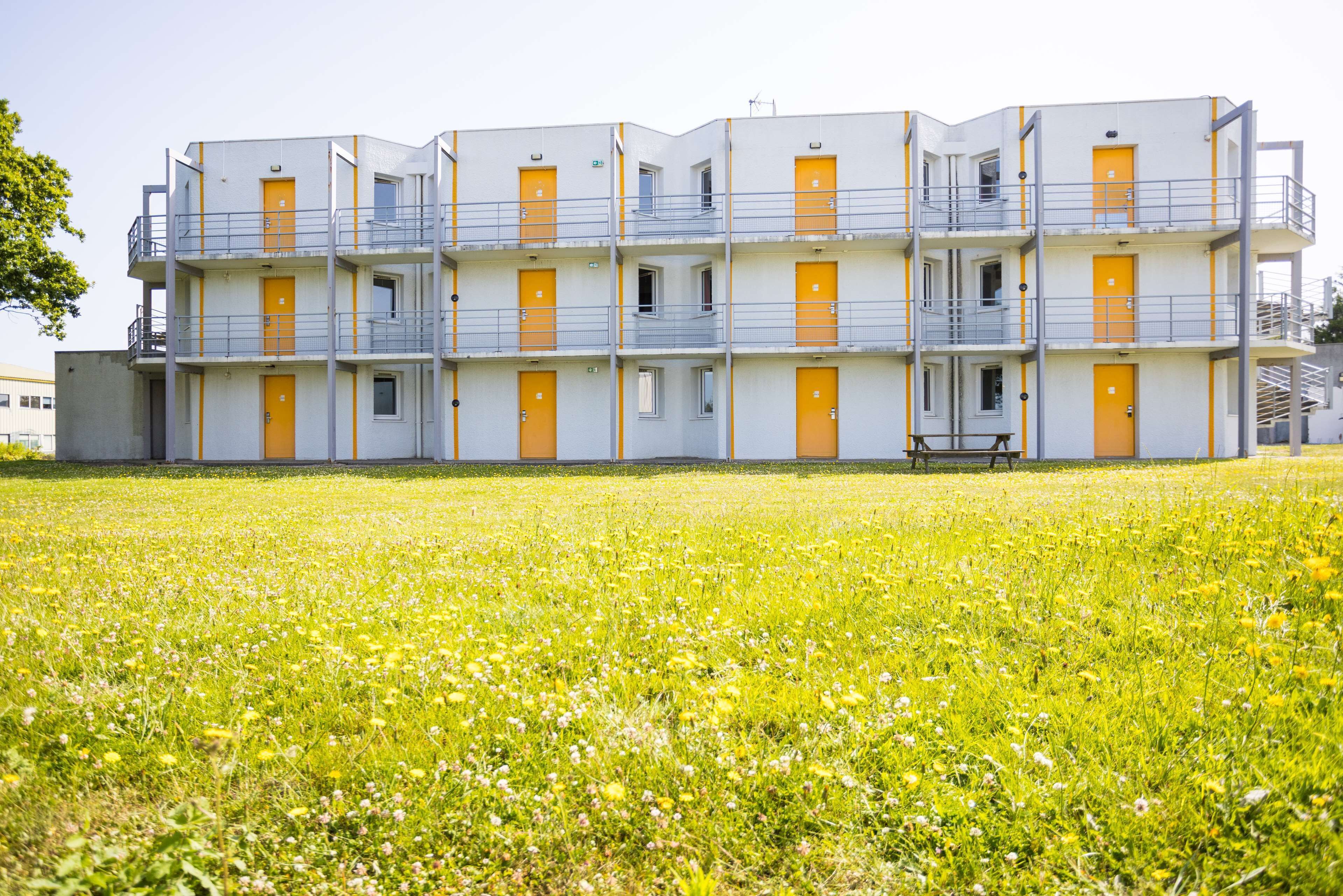 Een meerhoog gebouw met balkons en oranje deuren, omgeven door een grasveld.
