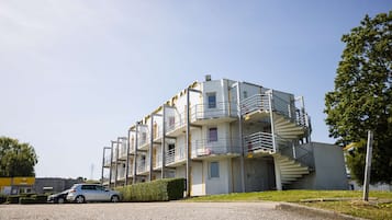 A multi-story residential building with a spiral staircase, a car parked in front, and a clear sky.