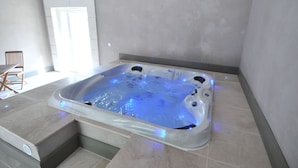 Un jacuzzi con luces LED azules, una silla y una puerta en una habitación con suelo de baldosas.