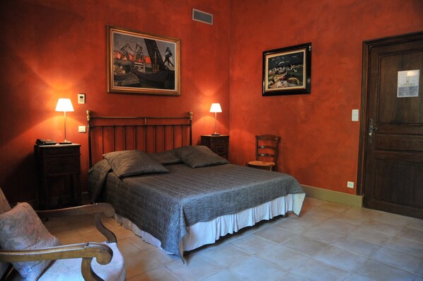 A bedroom with a wooden bed, two bedside tables with lamps, a chair, and two framed pictures on the walls.