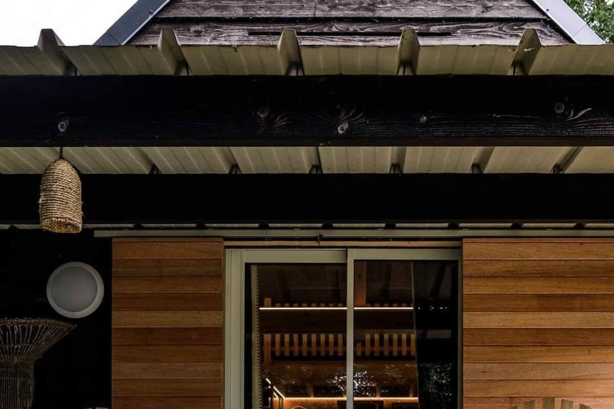 Une terrasse en bois avec deux fauteuils Adirondack et une petite table, un pot de fleurs suspendu et une grande fenêtre donnant sur l’intérieur.