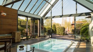Une piscine intérieure moderne avec des murs en verre, une terrasse en bois et un banc.