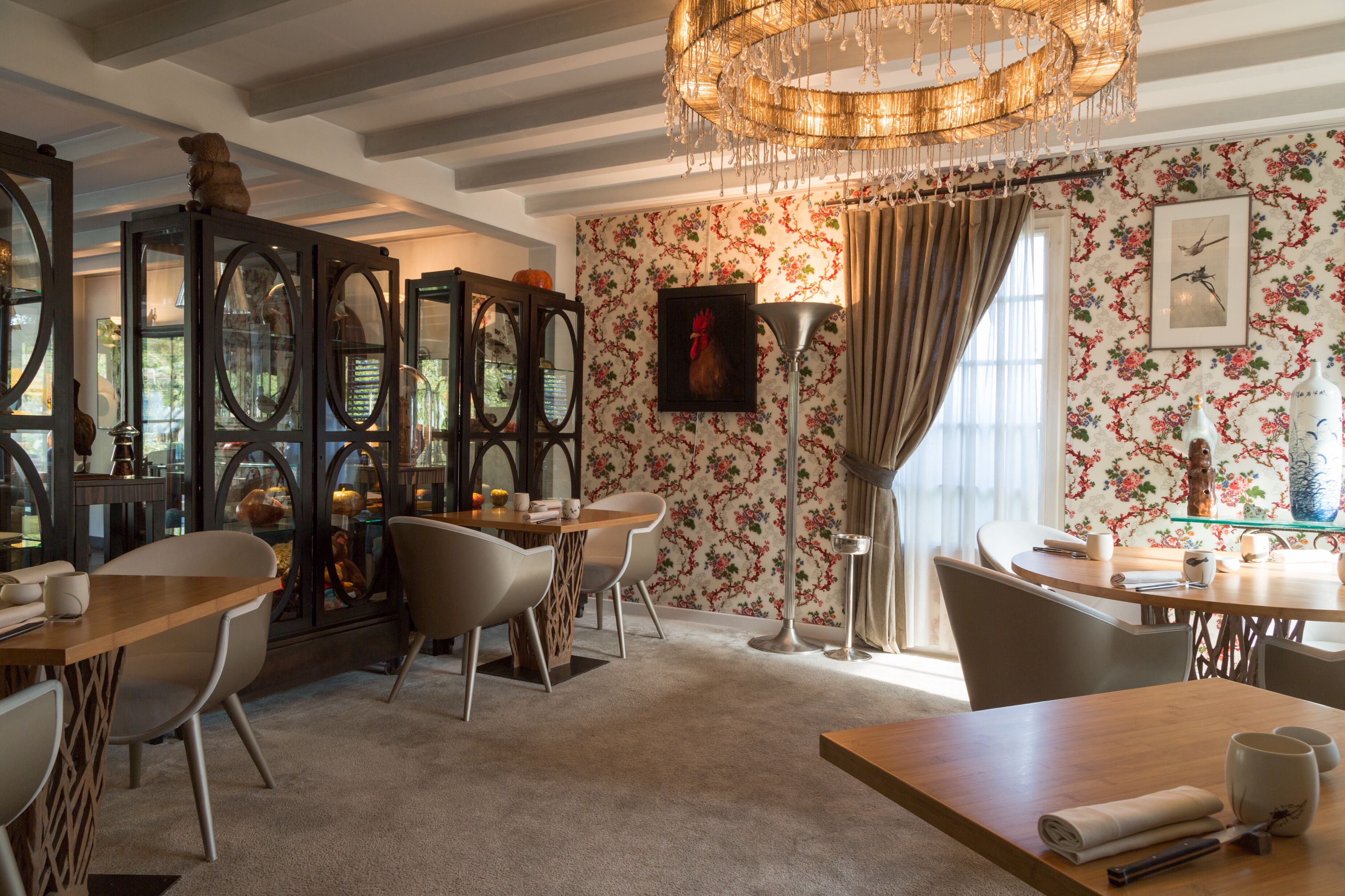 A dining area with a chandelier, floral wallpaper, and a wooden table with chairs.