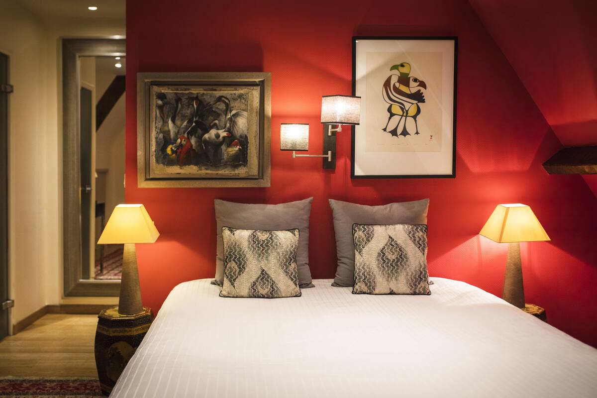 Une chambre d’hôtel avec un grand lit, deux lampes fixées au mur et deux œuvres d’art encadrées.