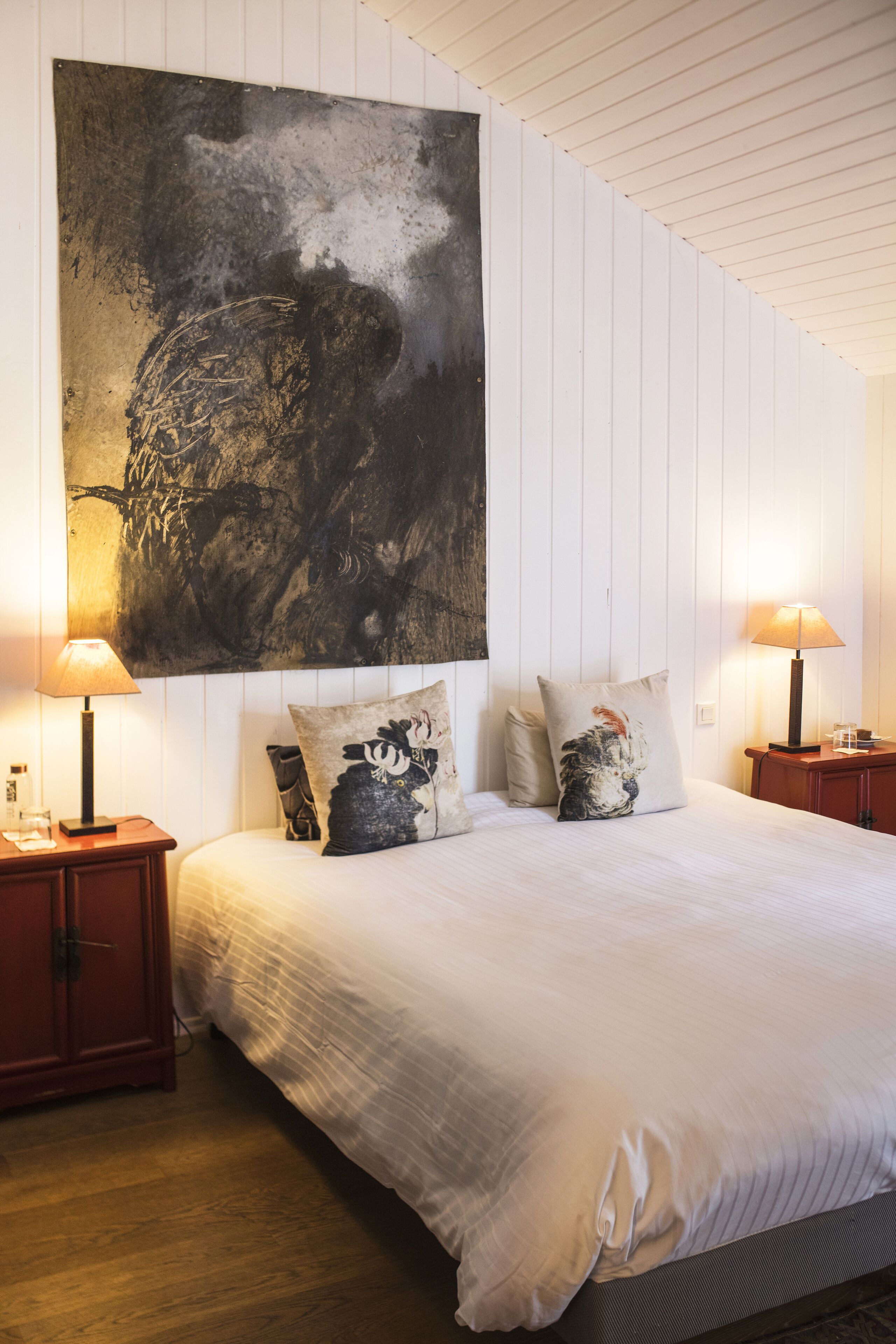 A bedroom with a large bed, two bedside tables, a wall-mounted painting, and two lamps.