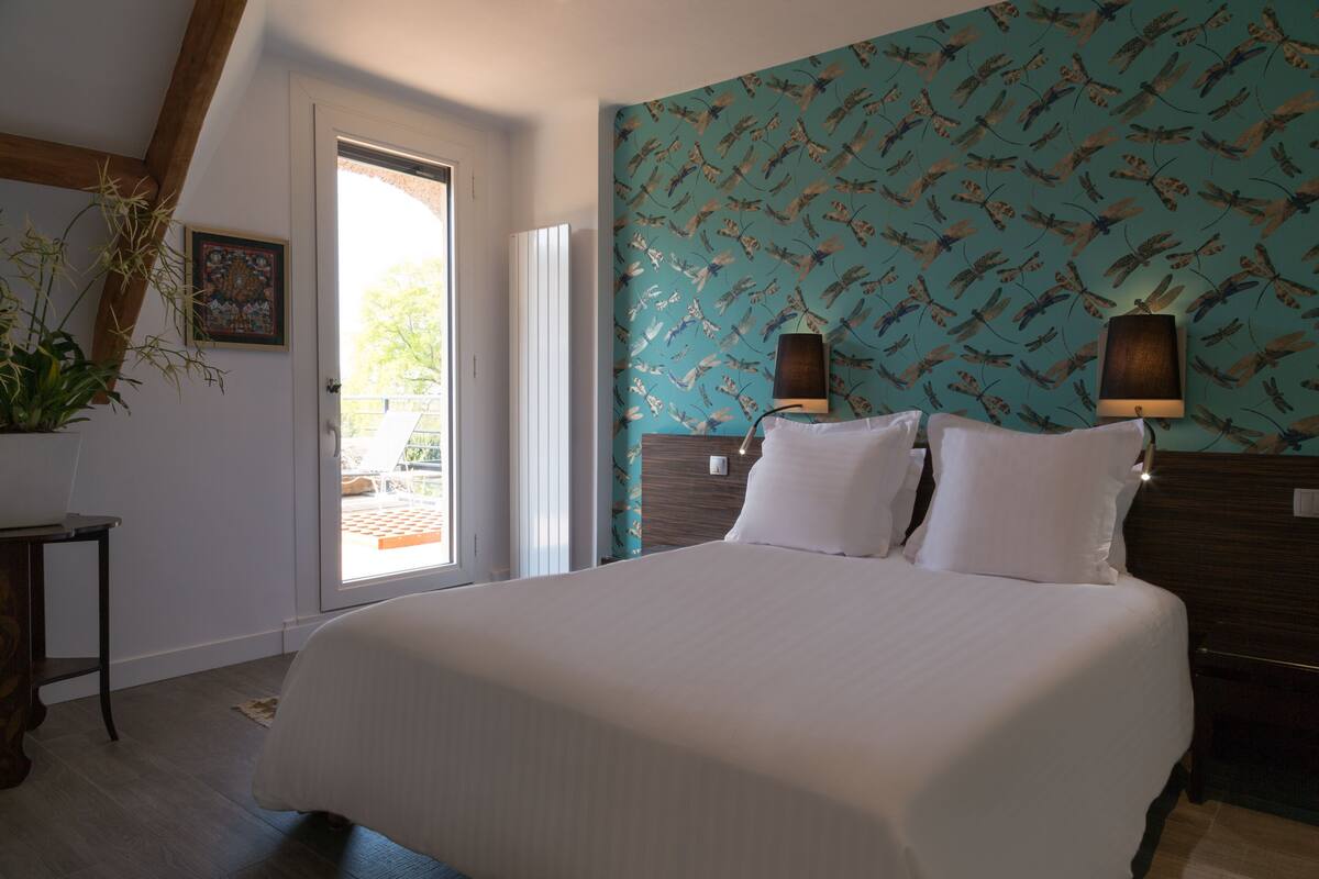 Une chambre à coucher avec un grand lit, une tête de lit en bois, deux lampes fixées au mur et un papier peint à motifs.