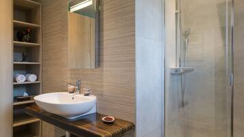 A modern bathroom with a large white sink, a mirror, and a glass-enclosed shower.