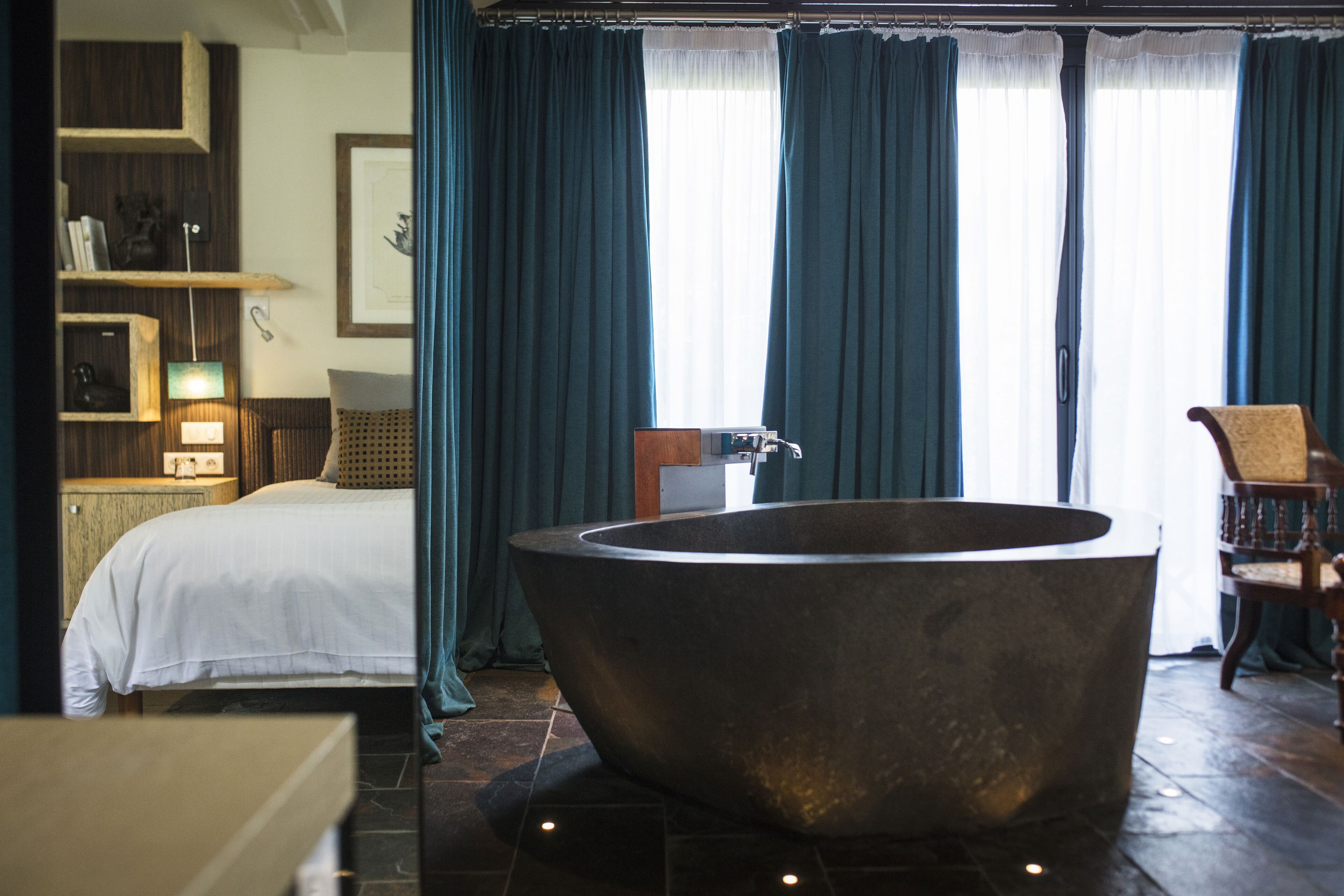 Un baño moderno con una bañera independiente grande, una cama con ropa de cama blanca y una silla de madera.