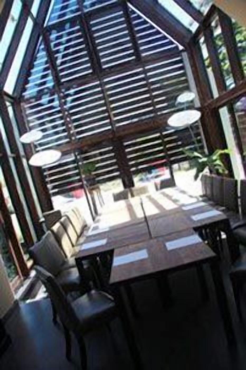 A covered outdoor seating area with tables and chairs, a glass ceiling, and a view of the street.