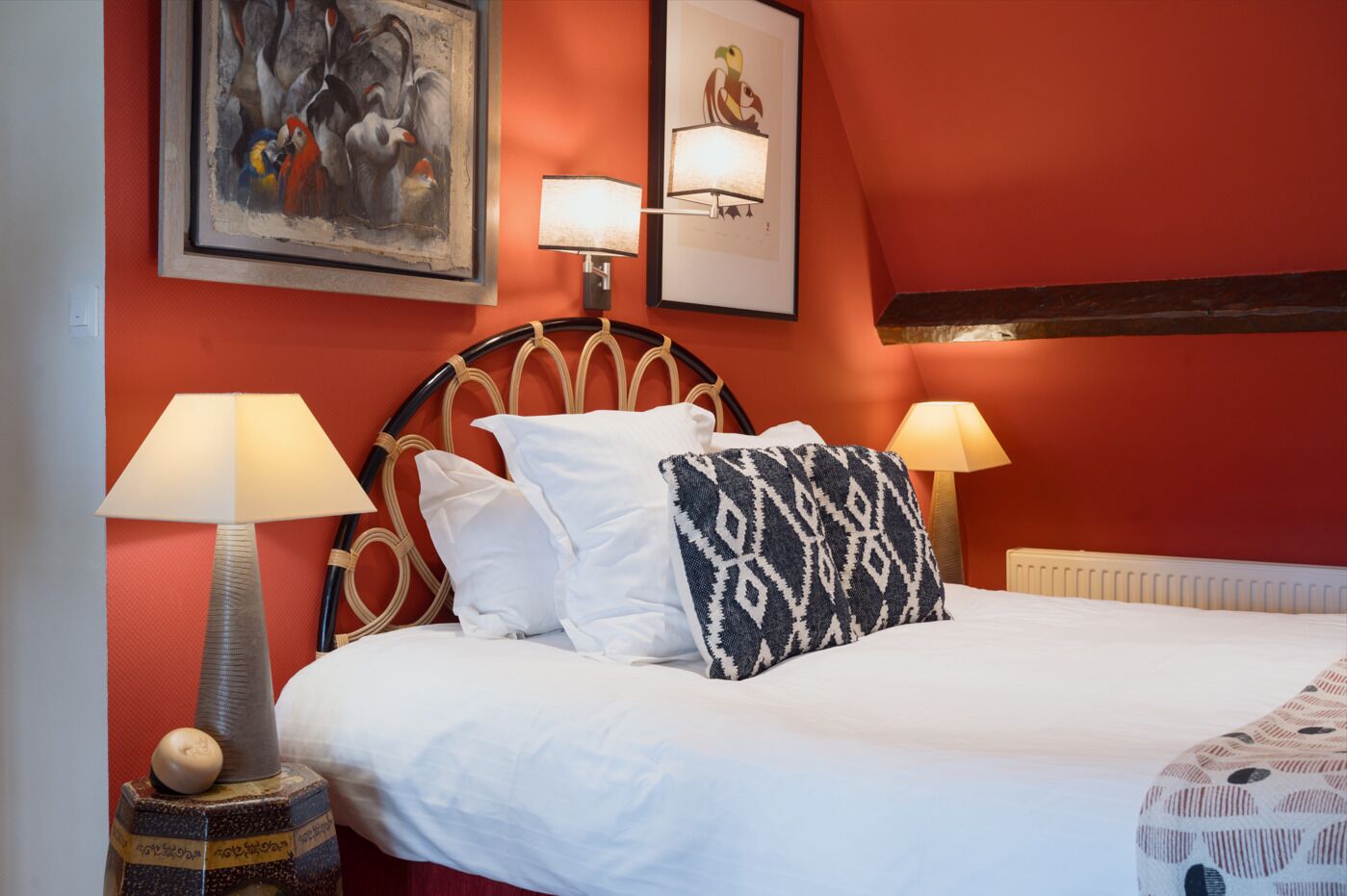 A hotel room with a bed, two wall-mounted lamps, a framed artwork, and a patterned throw pillow.