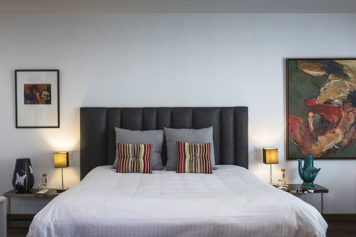 Un lit bien fait, avec des oreillers à rayures, une tête de lit sombre et un tableau encadré accroché au mur.