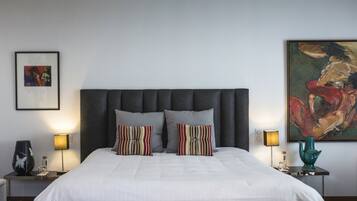 A neatly made bed with a grey upholstered headboard, two bedside tables with lamps, and a large abstract painting on the wall.