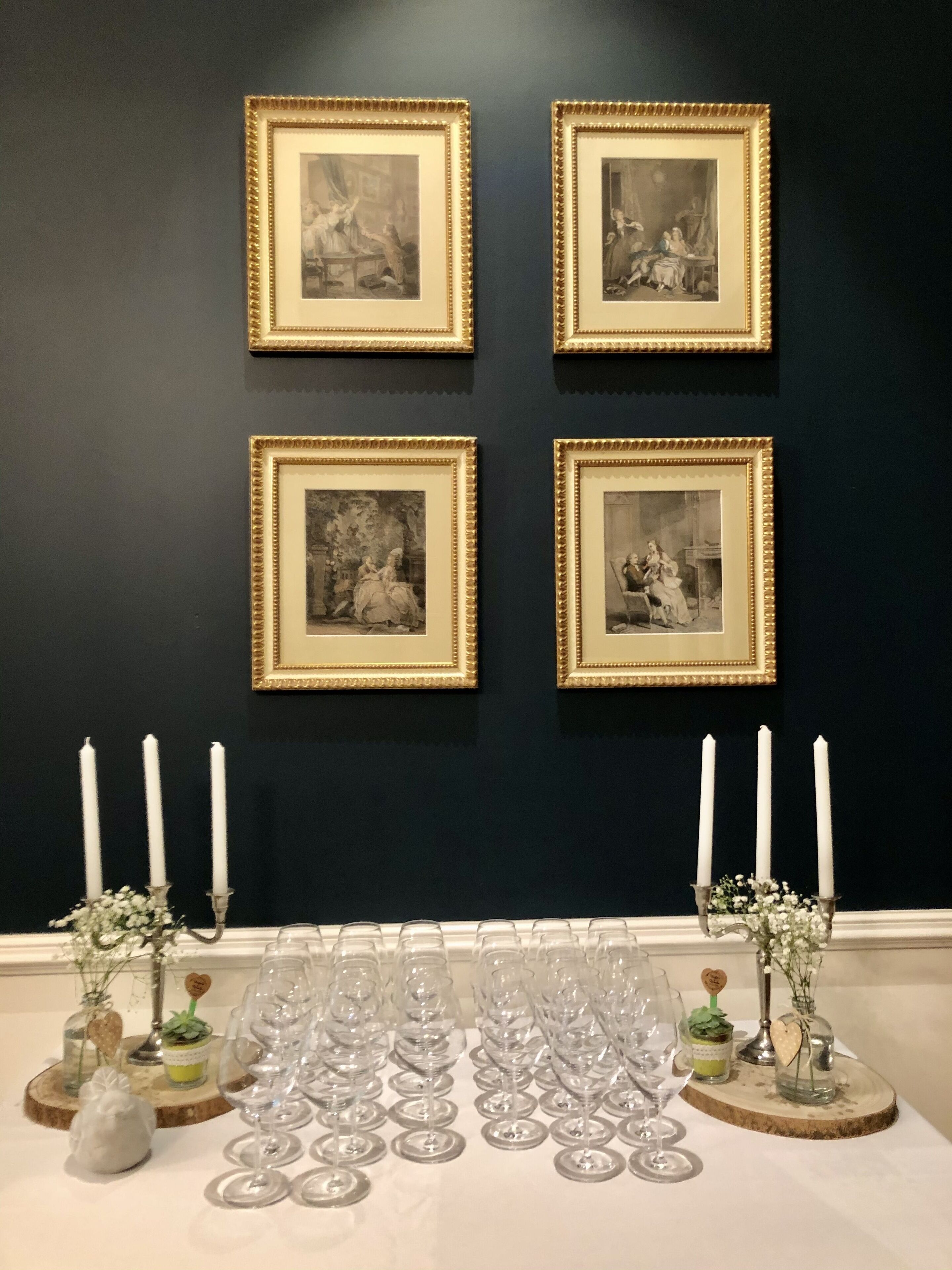 A wall with four framed black and white photographs, a table with wine glasses and candles, and decorative vases.
