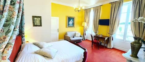 Een hotelkamer met een bed, een bureau, een stoel, een lamp en een raam met gordijnen.