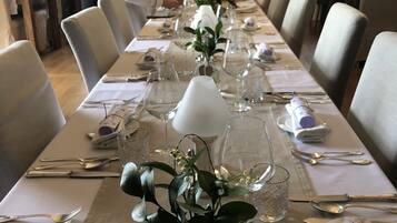 A long dining table set with chairs, a chandelier, and a mirror on the wall.