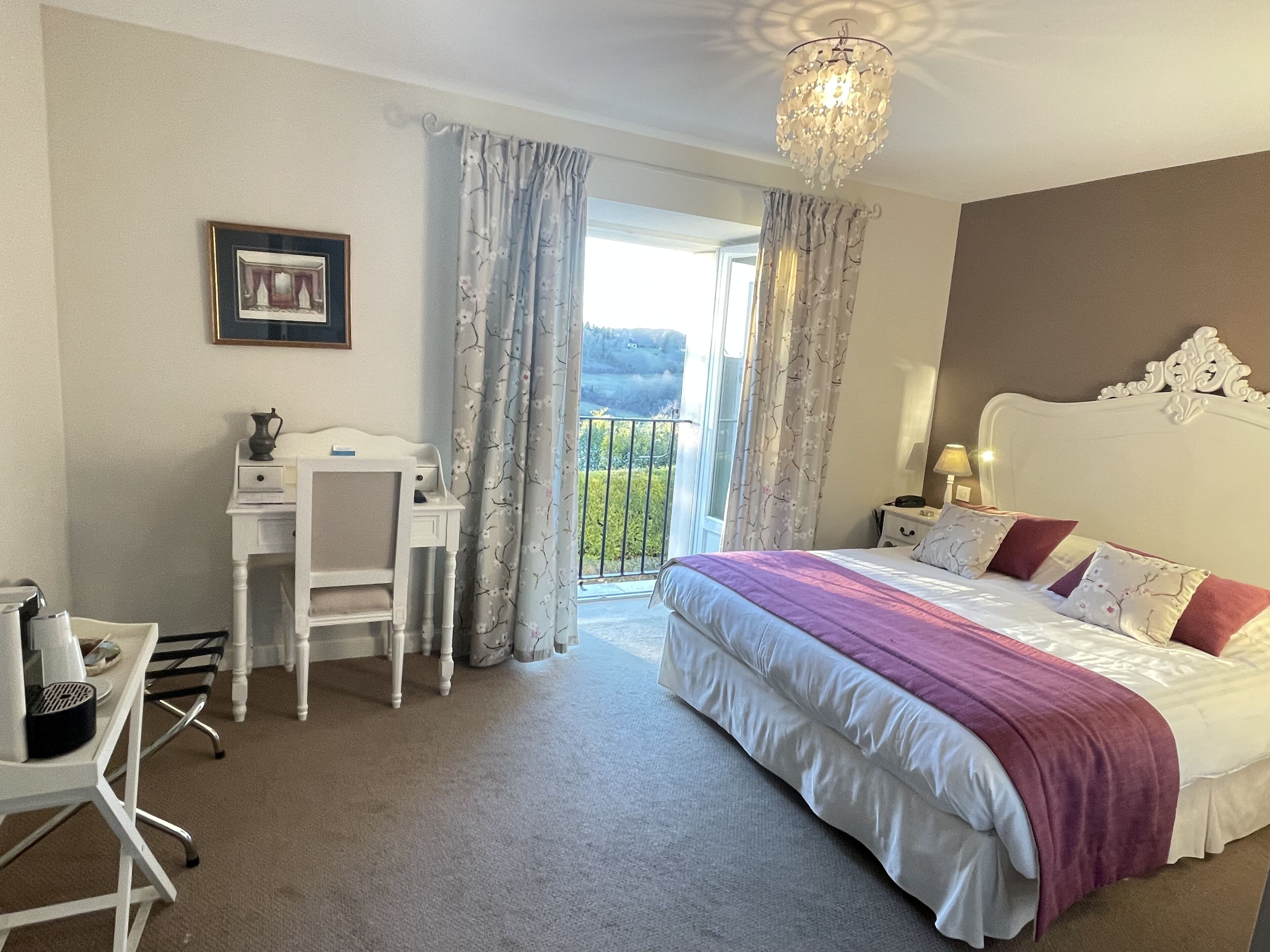 A hotel room with a bed, a desk, a chair, a picture frame, and a chandelier.