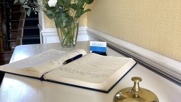A desk with a notebook, pen, a brass bell, and a vase with flowers.