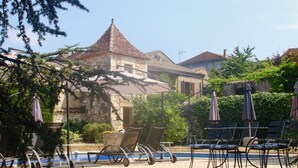 Un pati amb seients exteriors, una piscina i edificis de pedra amb teulades de rajola.
