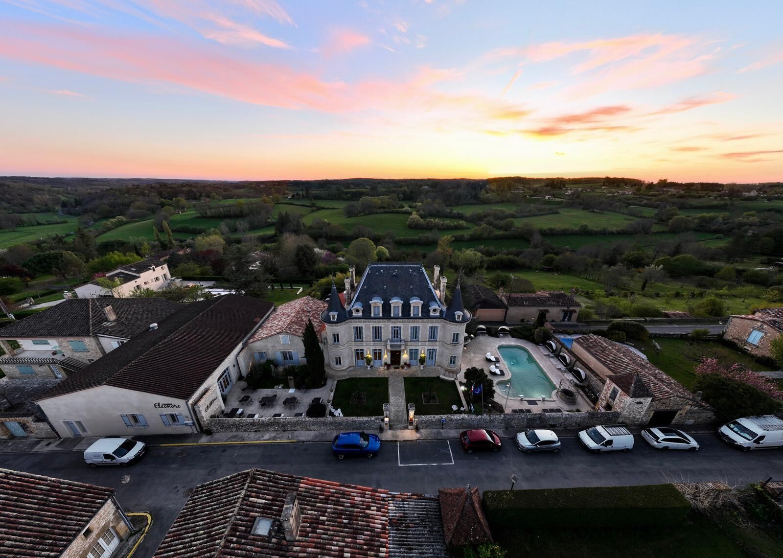 A large estate with a swimming pool, multiple cars, and a view of the surrounding countryside.