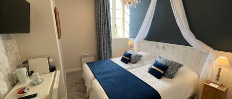 A bedroom with a bed, bedside tables, a desk with a chair, a television, and a chandelier.