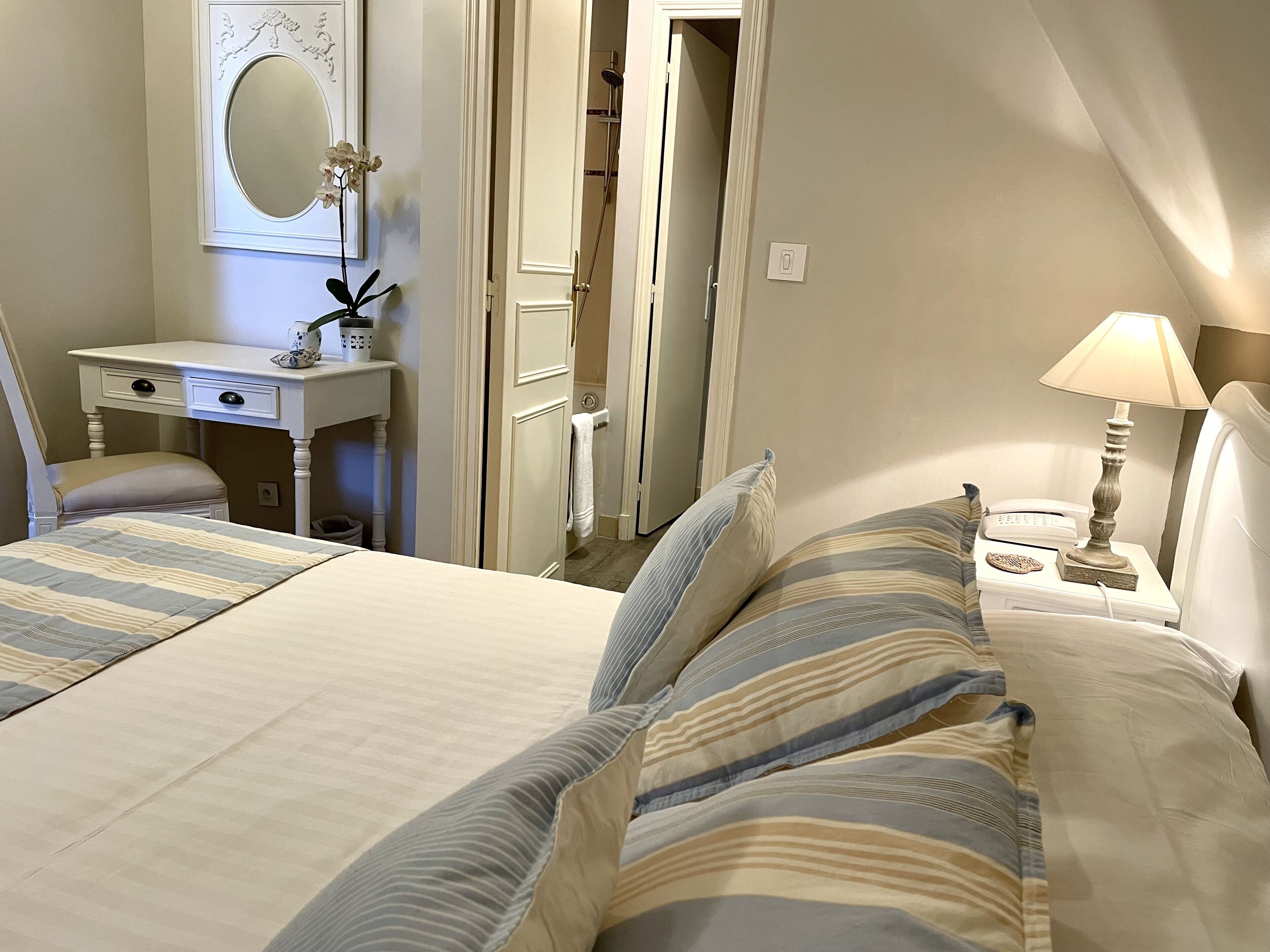 Une chambre à coucher comprenant un lit, une table de chevet avec une lampe, une commode, un miroir et une porte donnant sur une salle de bain.