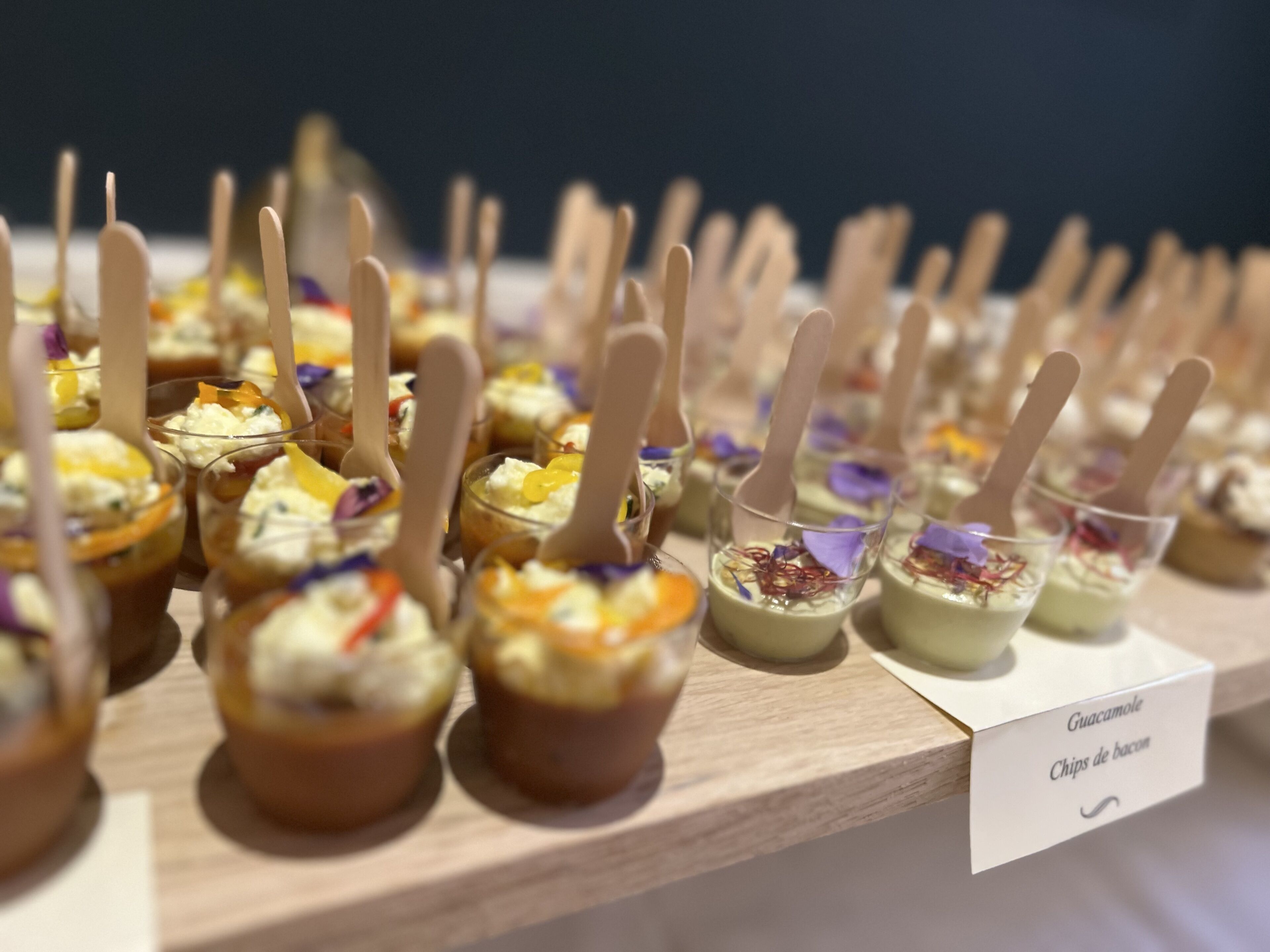 Een presentatie van etenswaren met houten stokjes, gelabeld 'Guacamole' en 'Chips de bacon'.