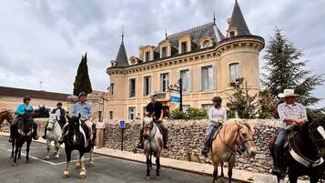 A group of people riding horses in front of a large, historic building with multiple towers and a stone wall.
