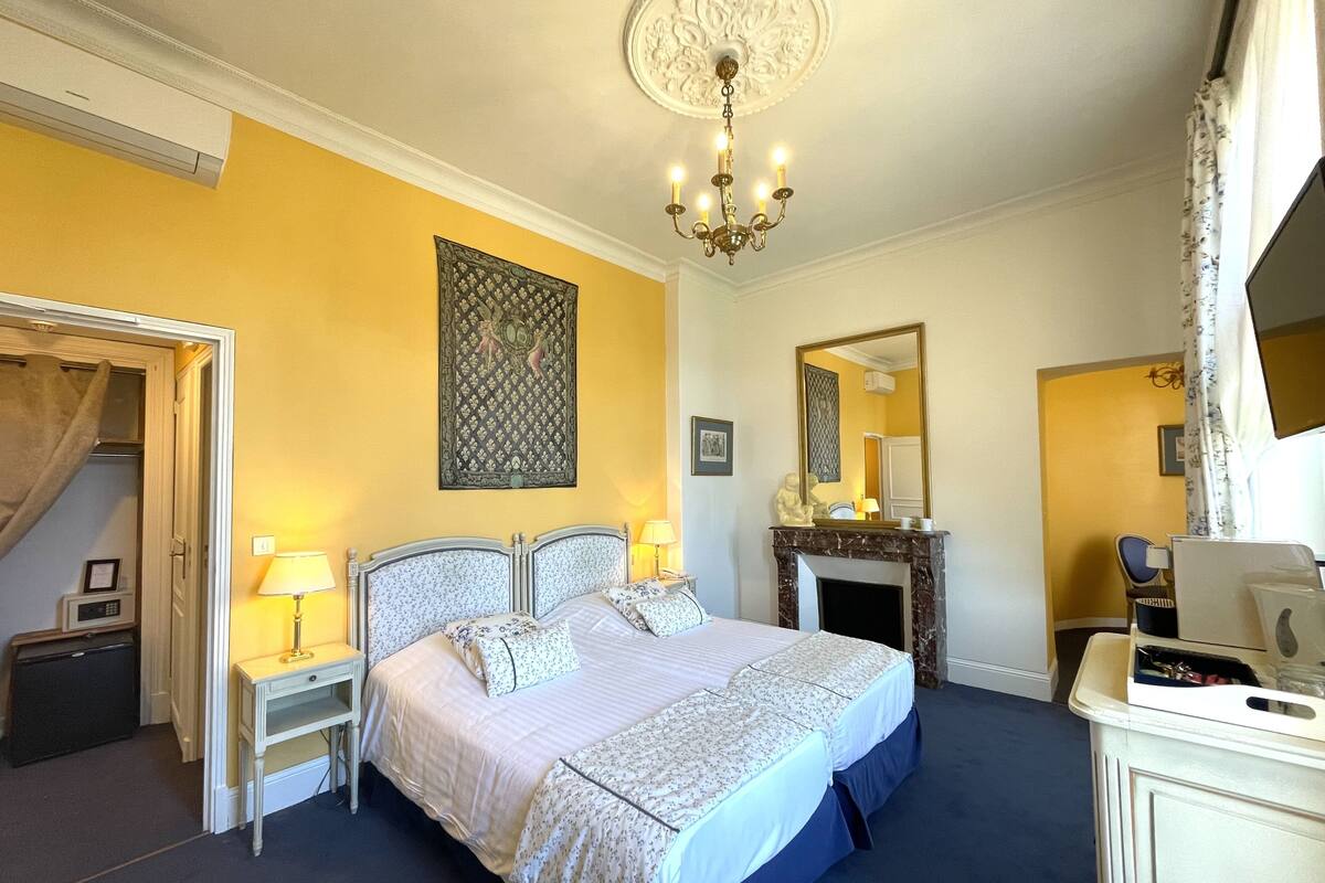 A bedroom with a bed, bedside tables, a mirror, a fireplace, and a chandelier.