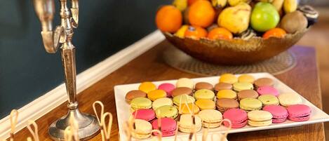 Una mesa con varios postres, incluyendo macarons y brownies, y un frutero al fondo.